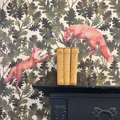 Two fabric fox decals leaping across a green oak-leaf wallpaper backdrop, displayed above a black cast-iron fireplace with three vintage &